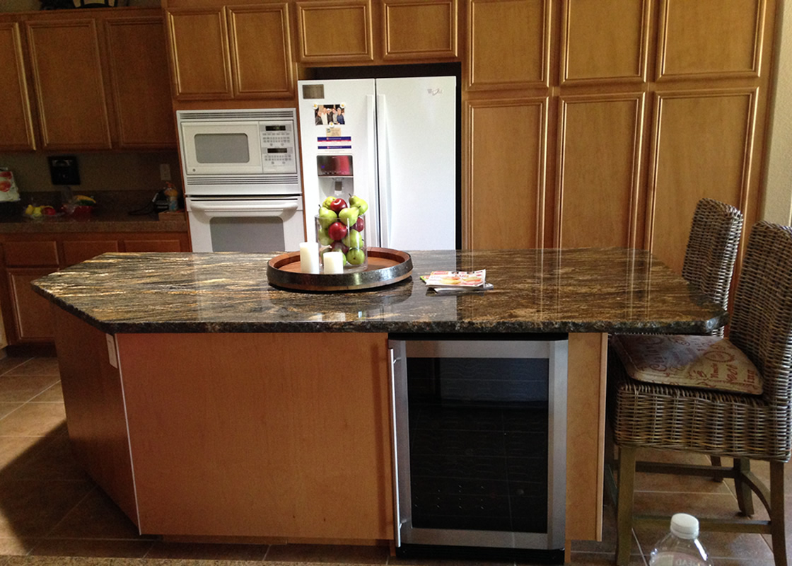 A picture of a kitchen Island, with cabinets and a refrigerator in the backrgound
