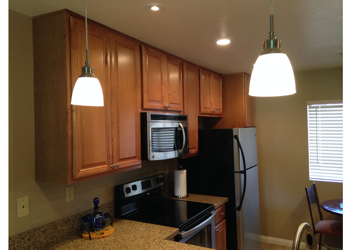 A picture of the kitchen, showing the microwave, stove/oven, refrigerator, cabinets, and lights.
