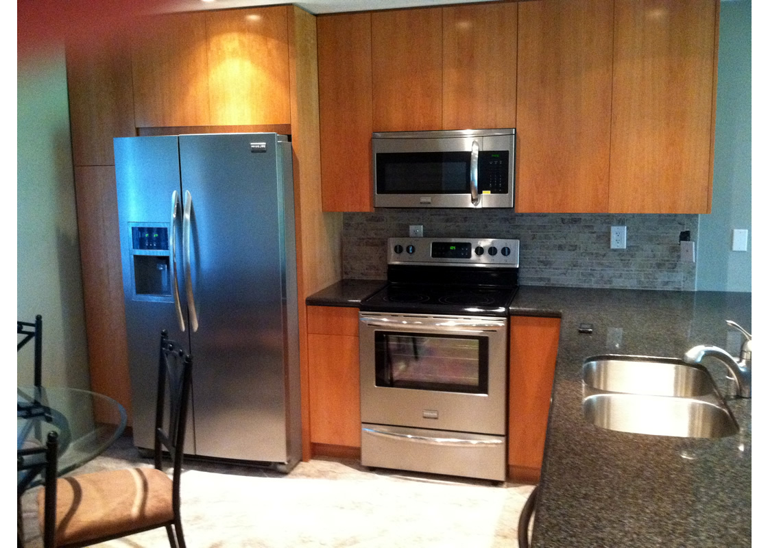 A picture of the kitchen, showing the microwave, oven, refrigerator, and cabinets.