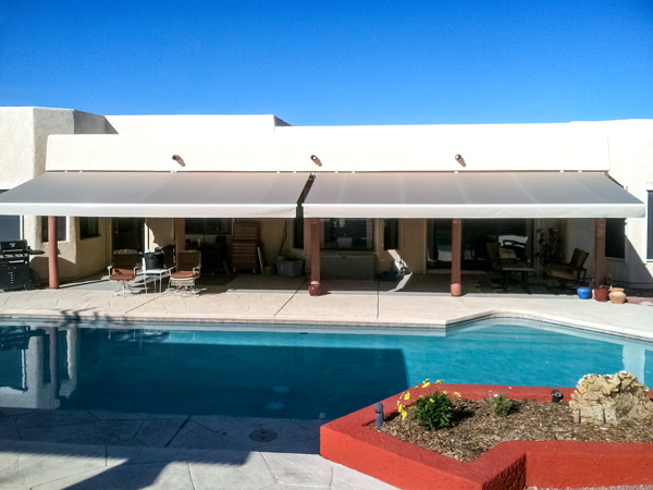 A picture of a pool and two awnings. The awnings are side by side and located behind the pool.